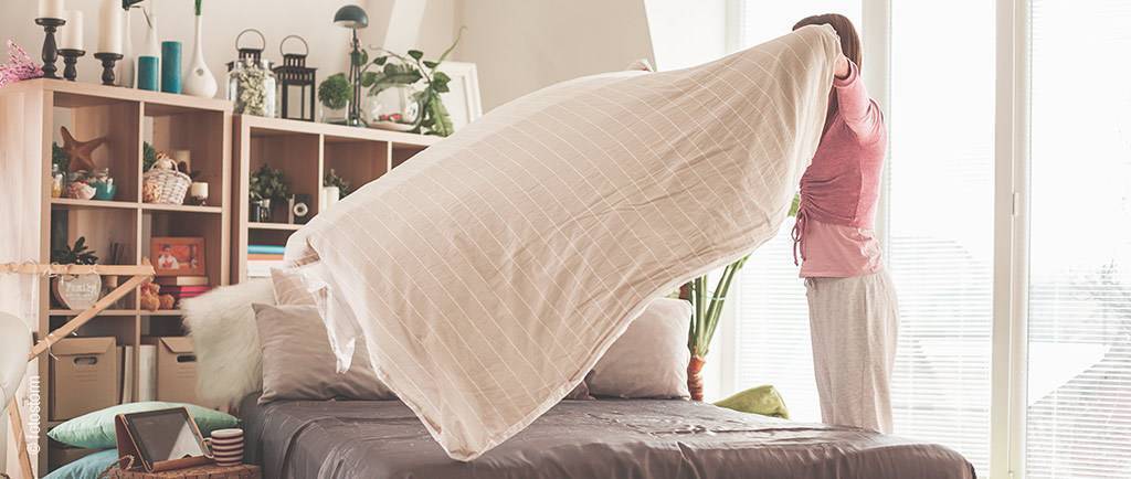 Foto: Eine Person wirft beim Bettenmachen die Tagesdecke über das Bett.