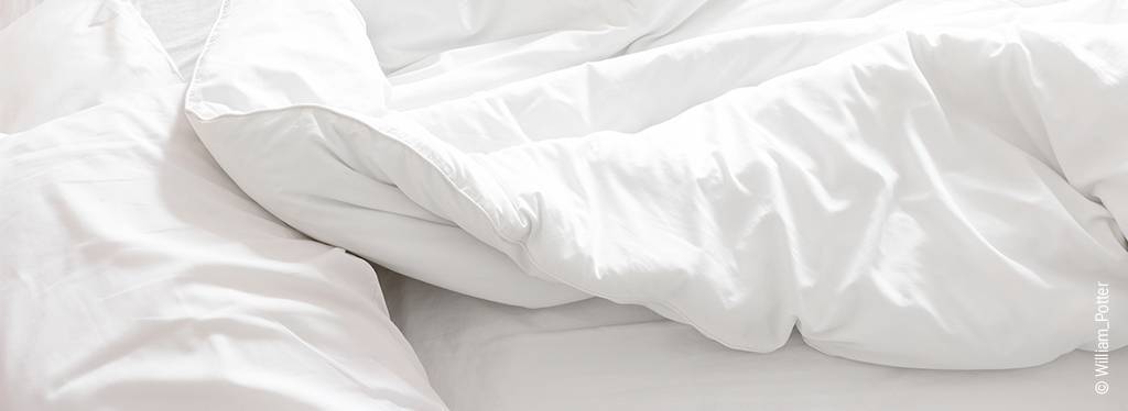 Foto: Weißes Kopfkissen und eine weiße Bettdecke auf einem Bett