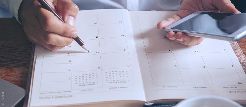 Foto: ein Kalender, darüber zwei Hände mit Stift und Smartphone