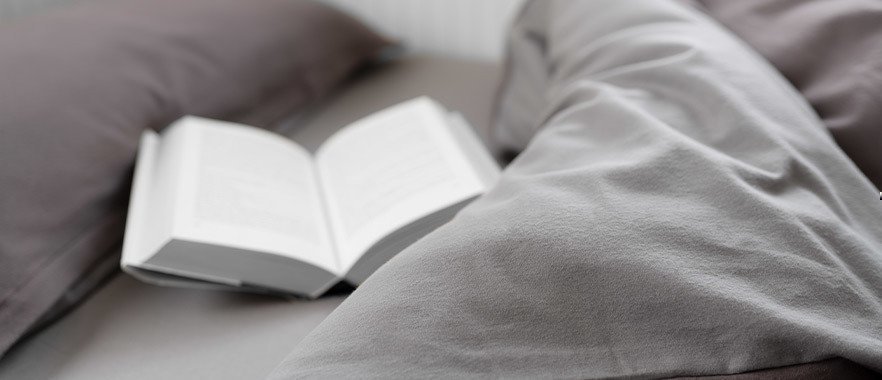 Foto: Nahaufnahme der grauen BODYGUARD® Flanell-Bettwäsche, ein Buch liegt aufgeschlagen mittendrin.