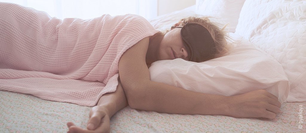 Foto: Eine Frau schläft am Tag im Bett, dabei trägt sie eine Schlafmaske.