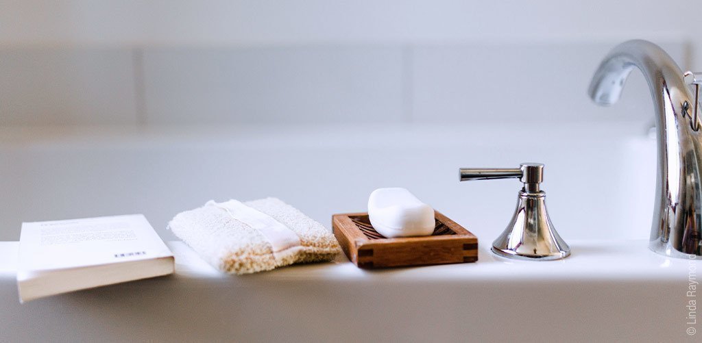 Foto: Ein Buch, ein Schwamm und Seife liegen am Rand einer Badewanne.