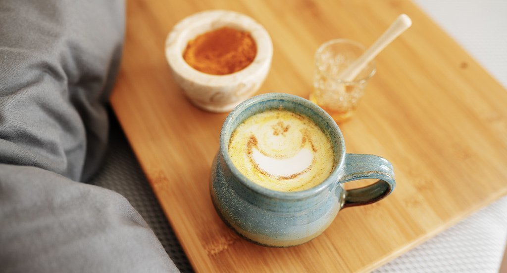 Foto: Eine blaue Tasse Milch mit Honig steht auf einem hölzernen Tisch.