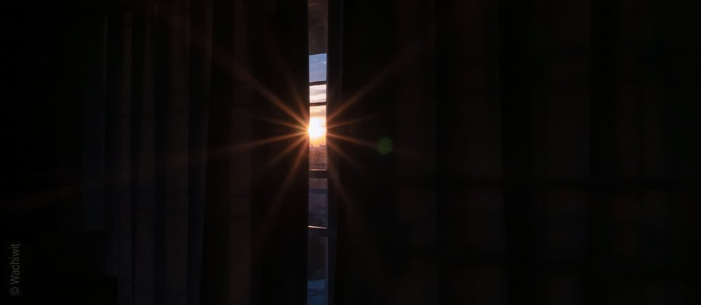 Foto: Verdunkelungsvorhänge vor einem Fenster, in der Mitte ist ein Spalt offen, der etwas Abendsonne durch das Fenster scheinen lässt.