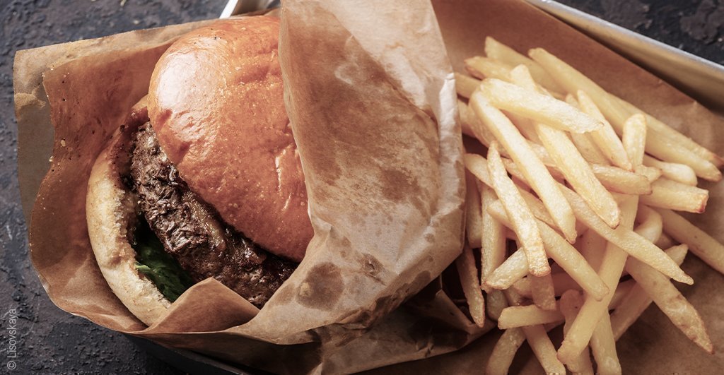 Foto: Ein Burger in fettigem Papier, daneben Pommes