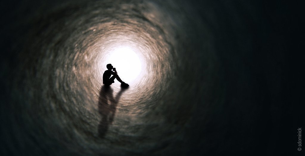 Foto: Blick durch eine dunkle Röhre in die am Ausgang helles Licht fällt. Die Silhouette einer sitzenden Person am Ende der Röhre ist zu erkennen.