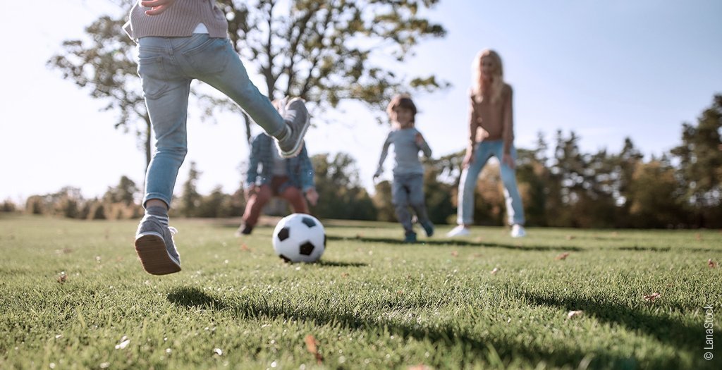 Foto: Kinder spielen auf einer Wiese Fußball.