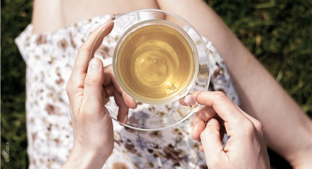 Foto: Vogelperspektive einer gefüllten Teetasse, die eine Frau über ihrem Schoß hält.