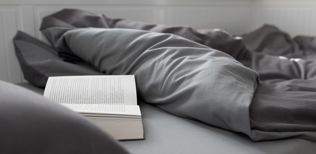 Foto: Ein Bett ist aufgeschlagen. Auf der Matratze liegt ein offenes Buch.