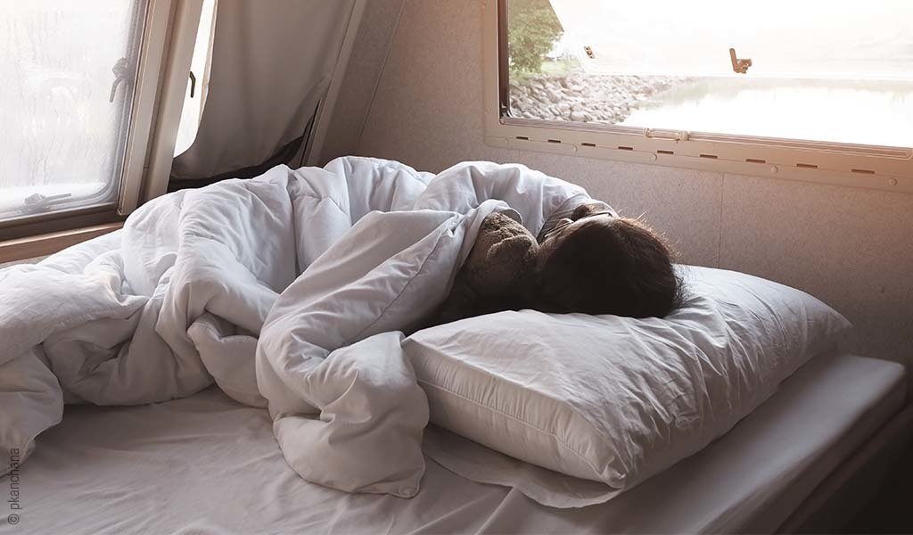 Foto: Eine Person liegt in einem Bett in einem Wohnmobil.