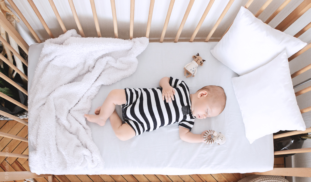 Foto in Vogelperspektive: Ein Baby schläft in Rückenlage auf einer Babymatratze 60x120 in einem Gitterbett.