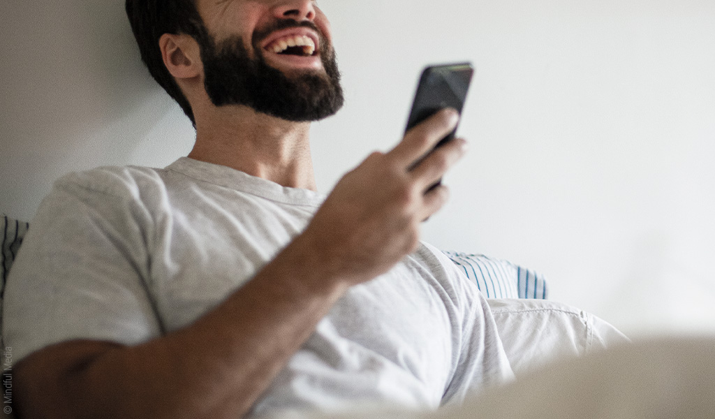Foto: Eine Person hält ein Smartphone vor sich und lacht.