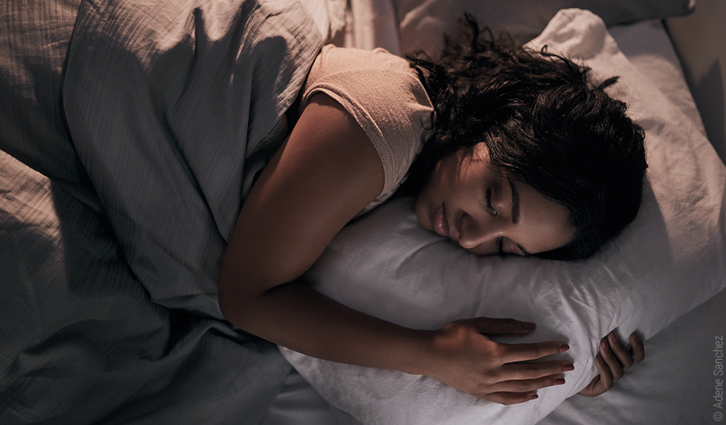 Foto: Eine Person liegt in Seitenschläfer-Position im Bett und hat die Augen geschlossen.