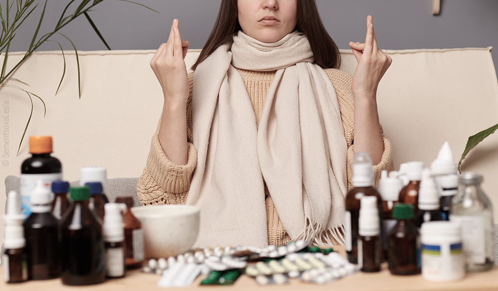 Foto: Hinter einem Tisch voller Pillen und Medizinfläschchen sitzt eine Person die Hände in Meditationsposition erhoben.