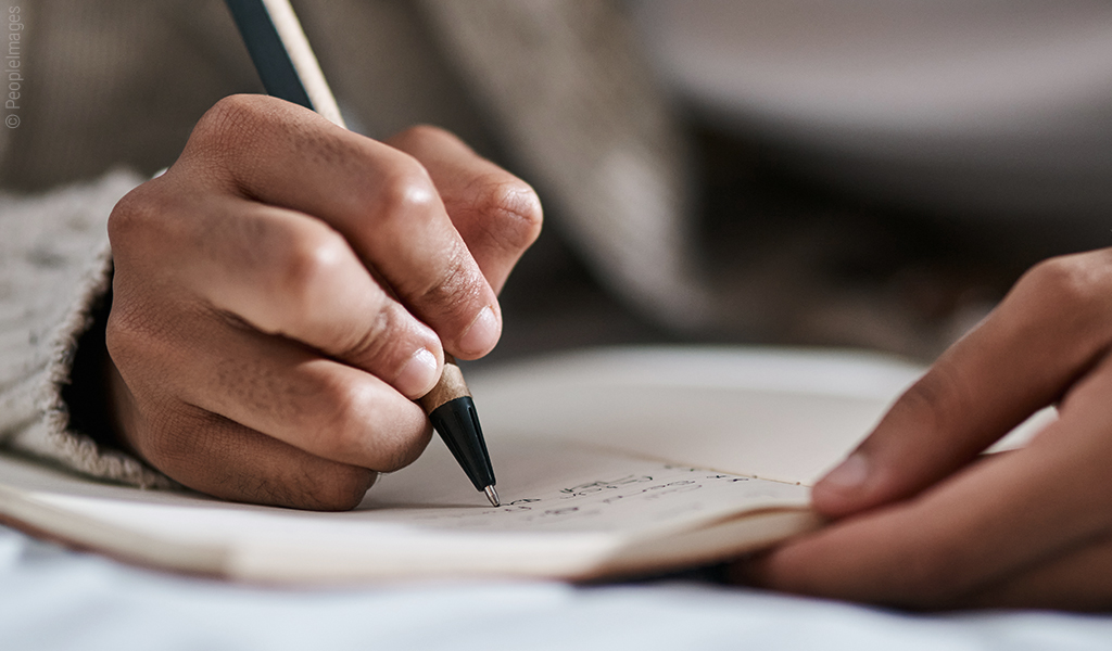 Foto: Eine Hand hält einen Stift und schreibt in ein Notizbuch.