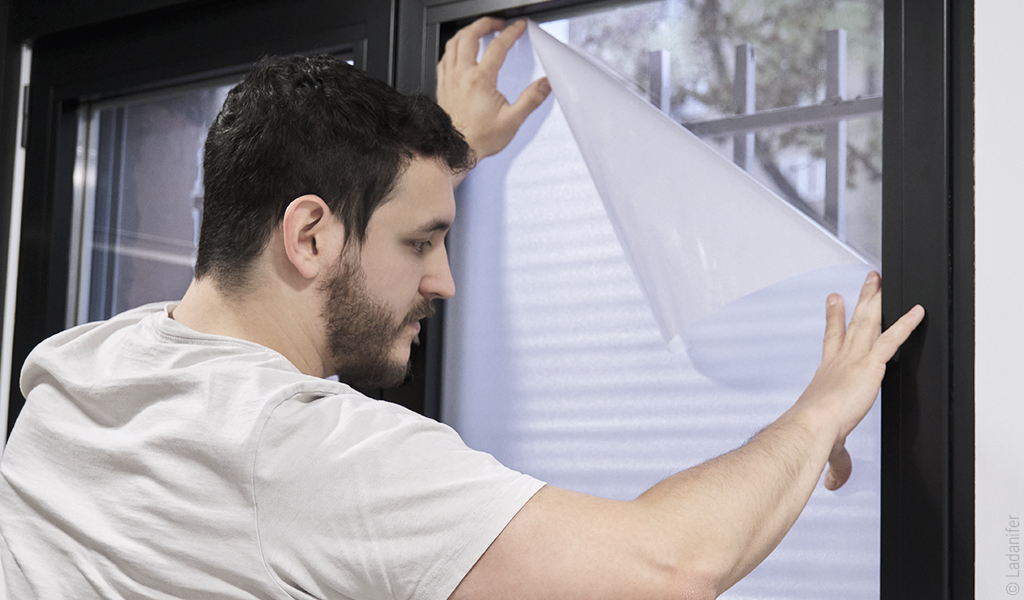 Foto: Eine Person befestigt eine Fensterfolie ans Fenster.