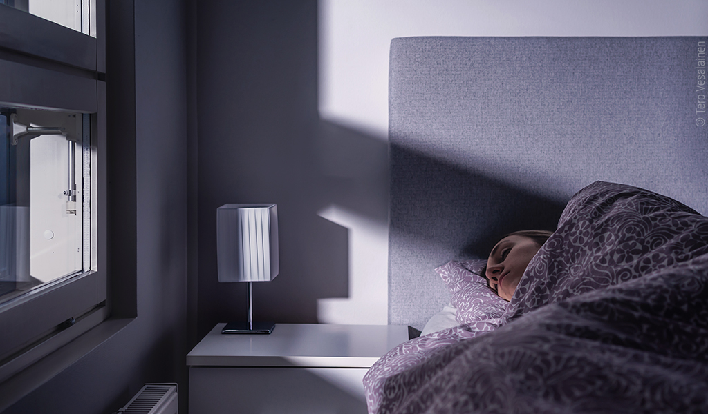 Foto: Eine Person schläft nachts im Bett, von draußen scheint es hell in das Schlafzimmer hinein.