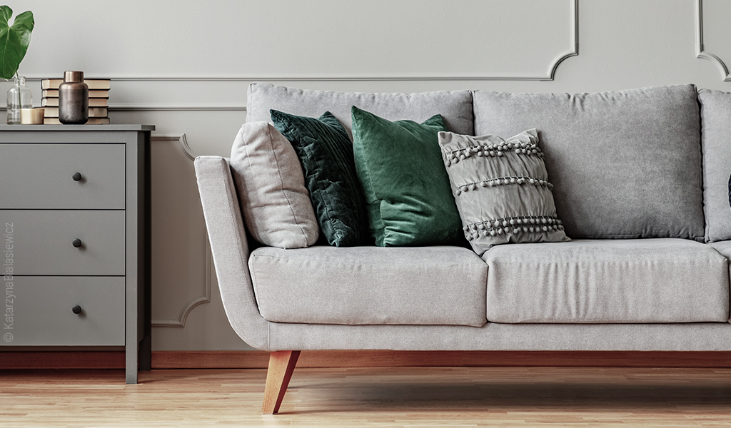 Foto: Eine Couch steht neben einer Kommode. Auf der Couch befinden sich mehrere quadratische Kissen in unterschiedlichen Farben.