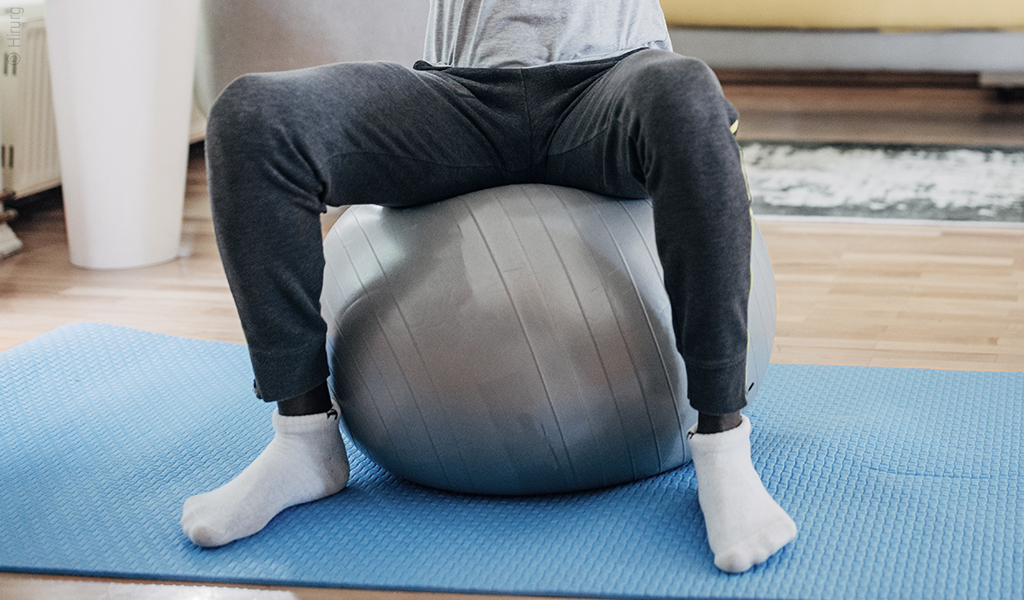 Foto: Eine Person sitzt mit gespreizten Beinen auf einem Gymnastikball.