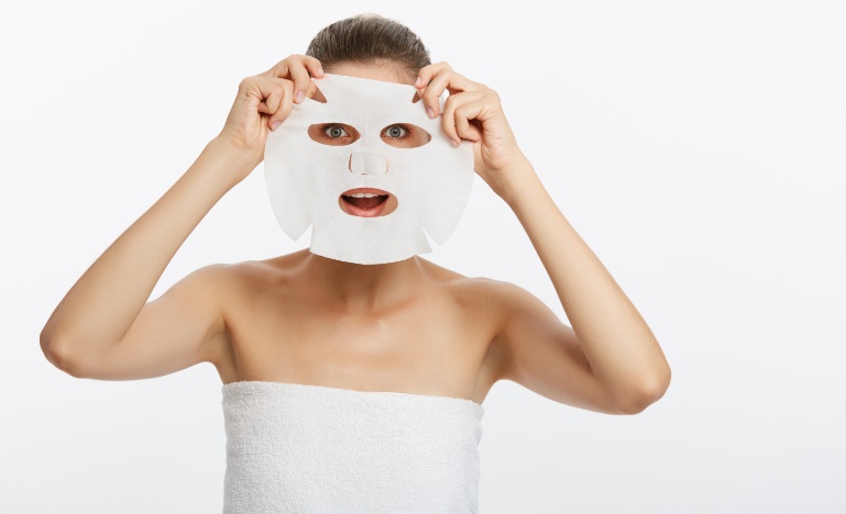 Mulher aplicando sheet mask sob o rosto.