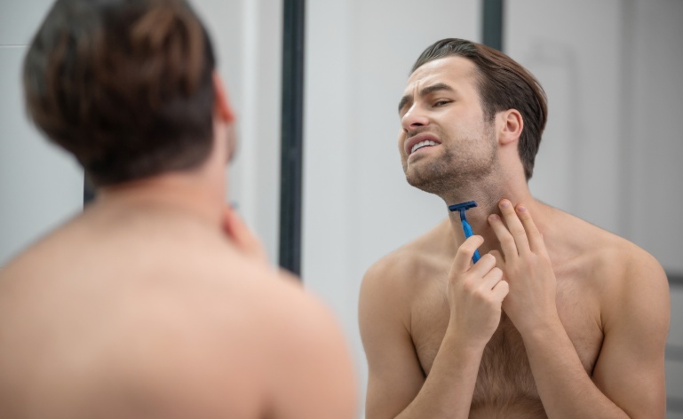 homem em frente ao espelho com lâmina de barbear passando na barba