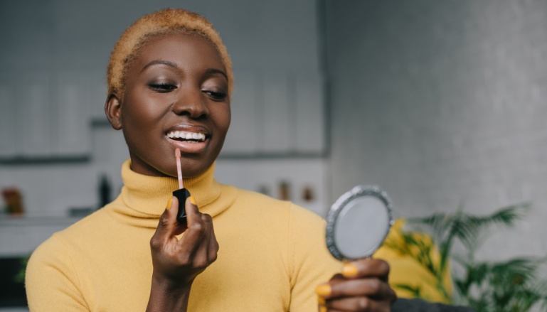 Mulher sorridente passando maquiagem para pele morena e negra.