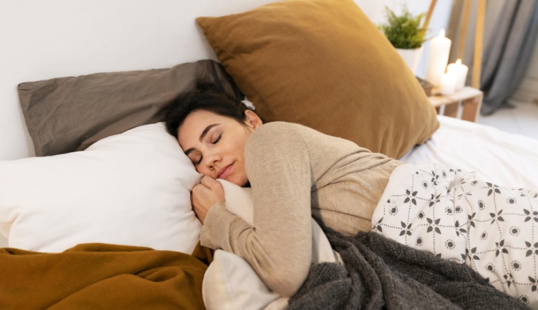 Mulher dormindo em uma cama aconchegante remete aos bons hábitos para evitar olheiras.