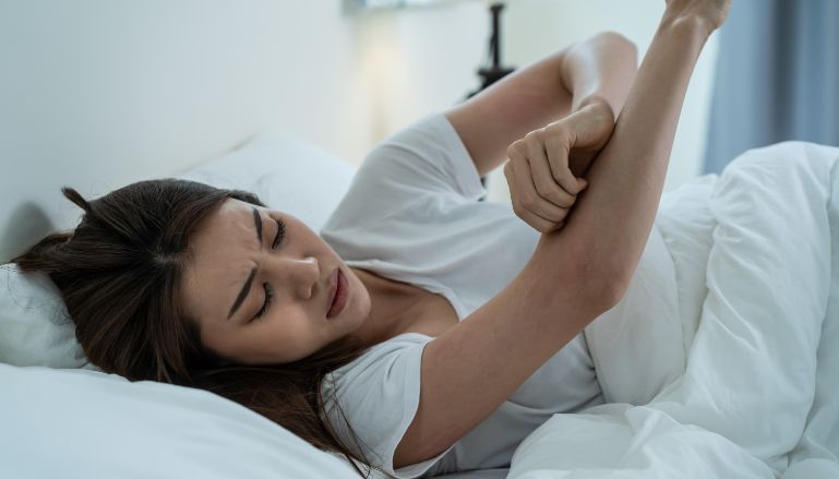 mulher deitada na cama coçando o braço