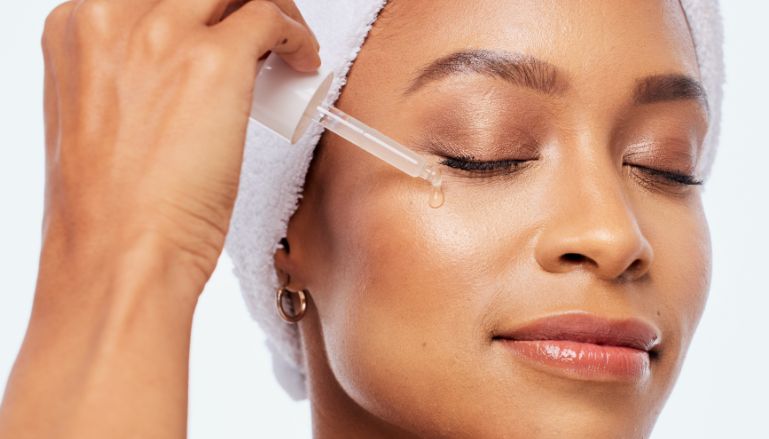 Mulher negra aplicando produto cosmético no rosto.