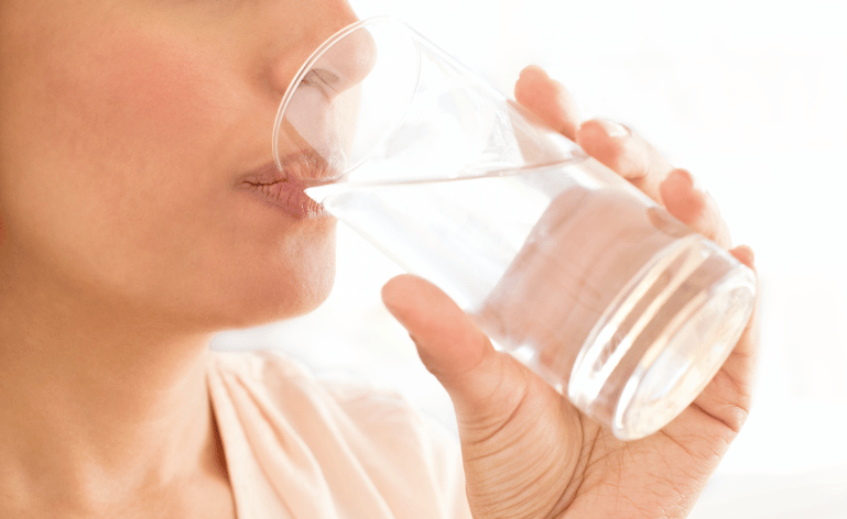 Mulher bebeneo água em um copo.