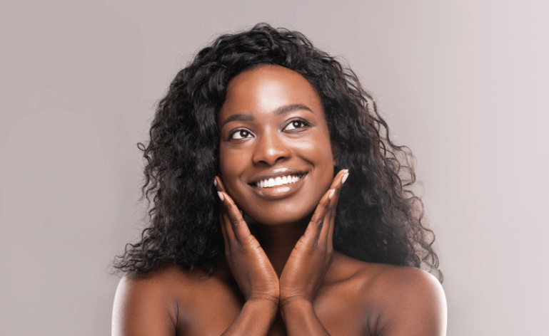 Mulher negra tocando o rosto e sorrindo após aplicar um antioxidante na pele.