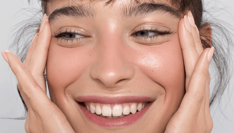 Mulher branca sorrindo e puxando o rosto com as mãos.