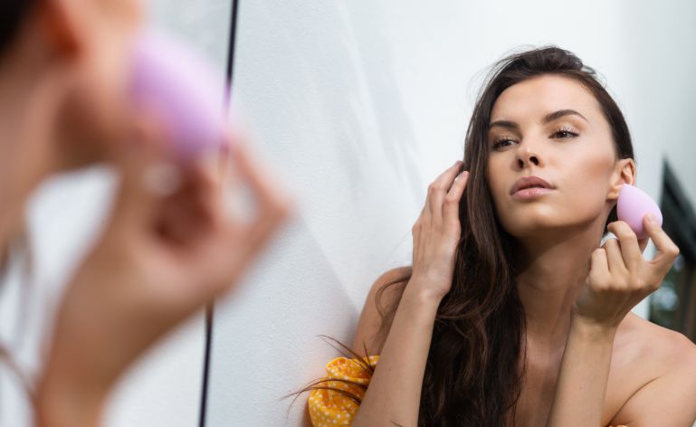 Mulher branca passando base em frente a um espelho