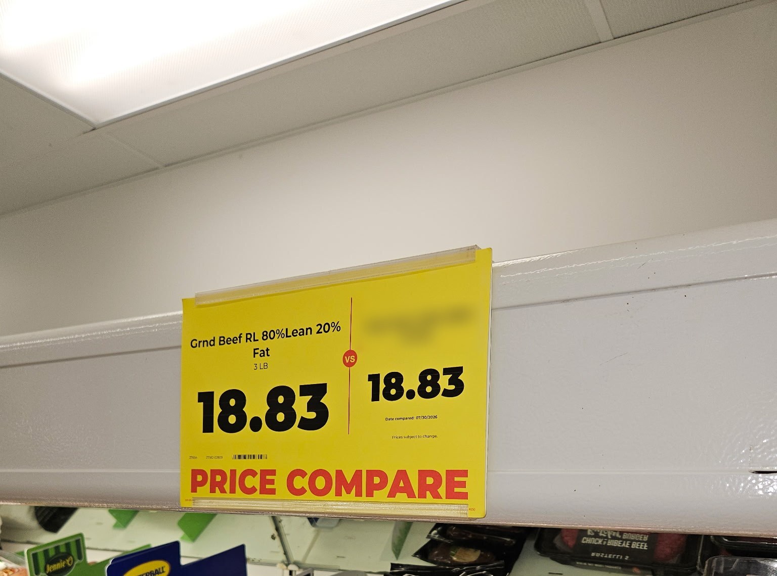 Price compare sign mounted on a meat case