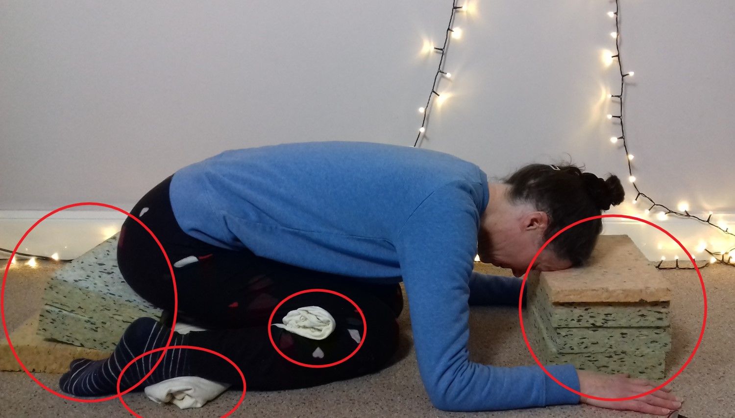 Image: Modifications for child's pose include bottom raised up on support, rolled towel under ankles, rolled towel behind knees, head resting on raised support. 