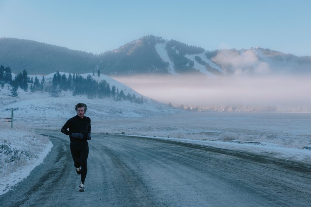 man running down a road with snowy fields and mountains behind him