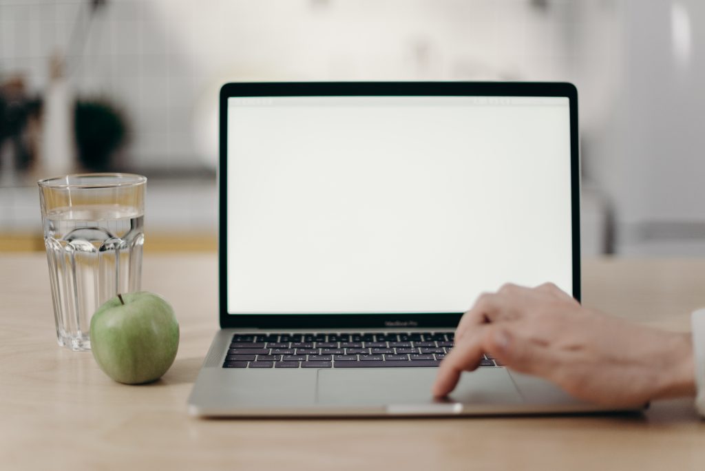 Laptop on desk next to a glass of water and an apple.