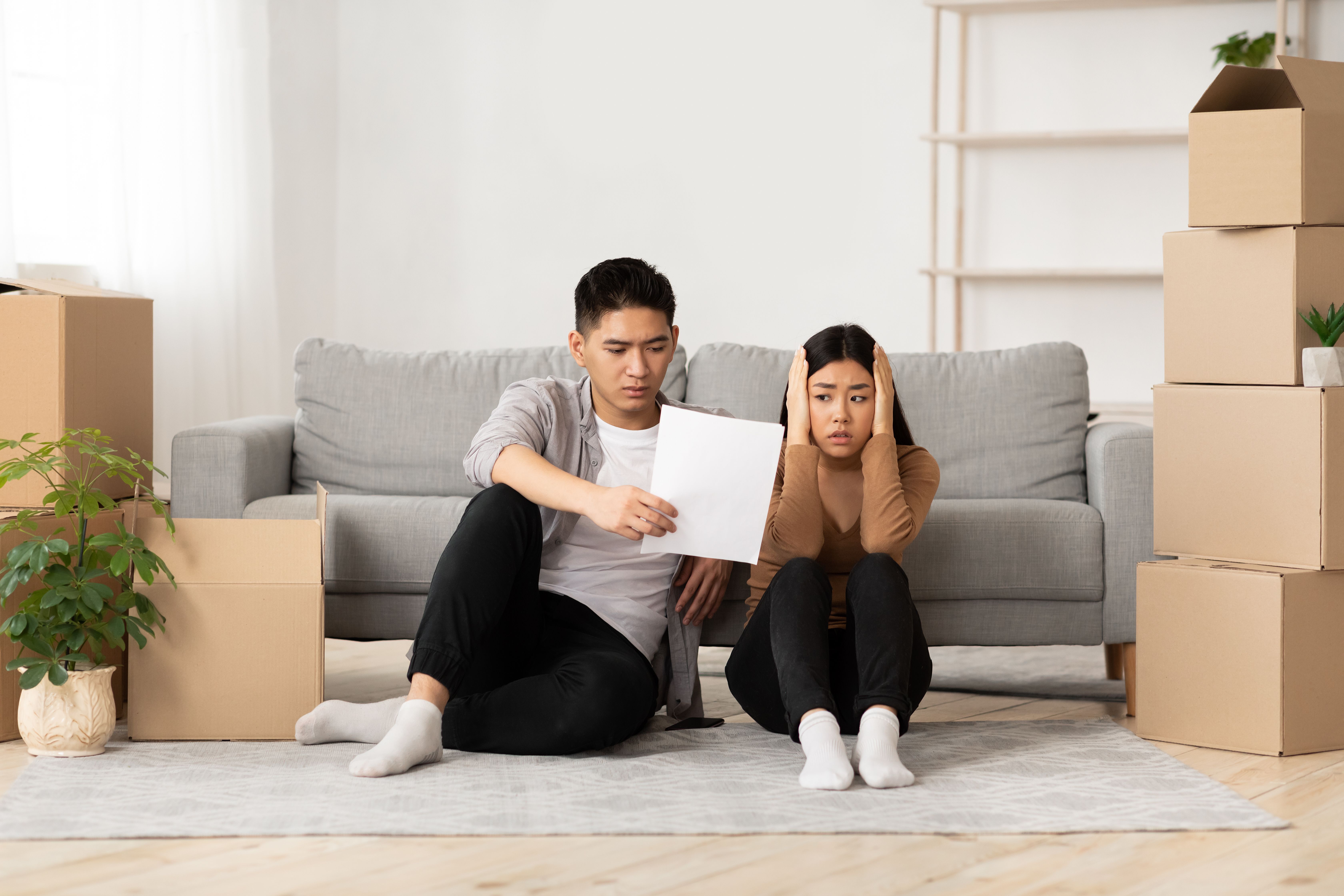 A scared couple looking at an eviction notice while sitting on the floor