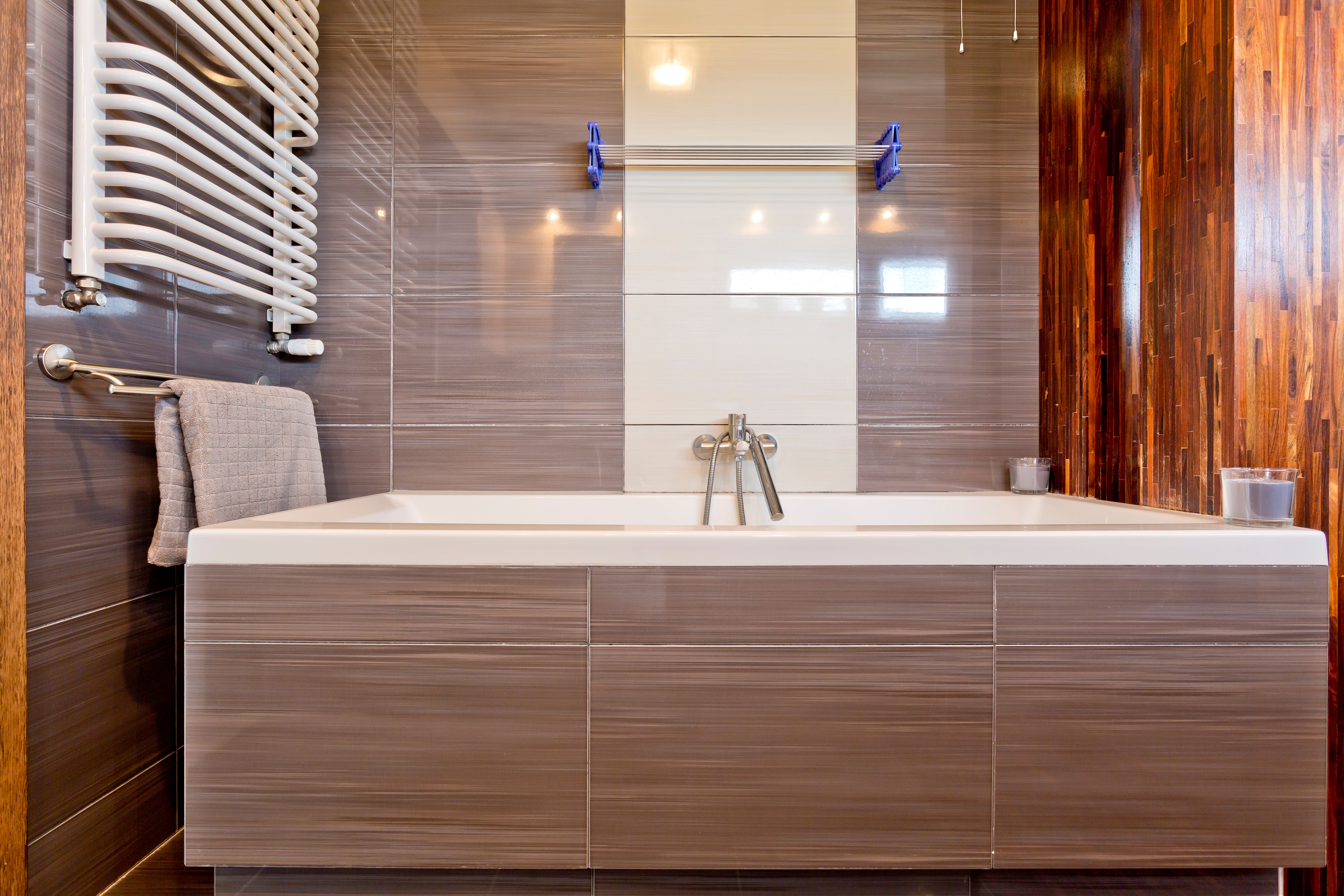 A radiator installed in a bathroom with a grey bathtub, a towel, modern fixtures and a wooden pillar
.jpg