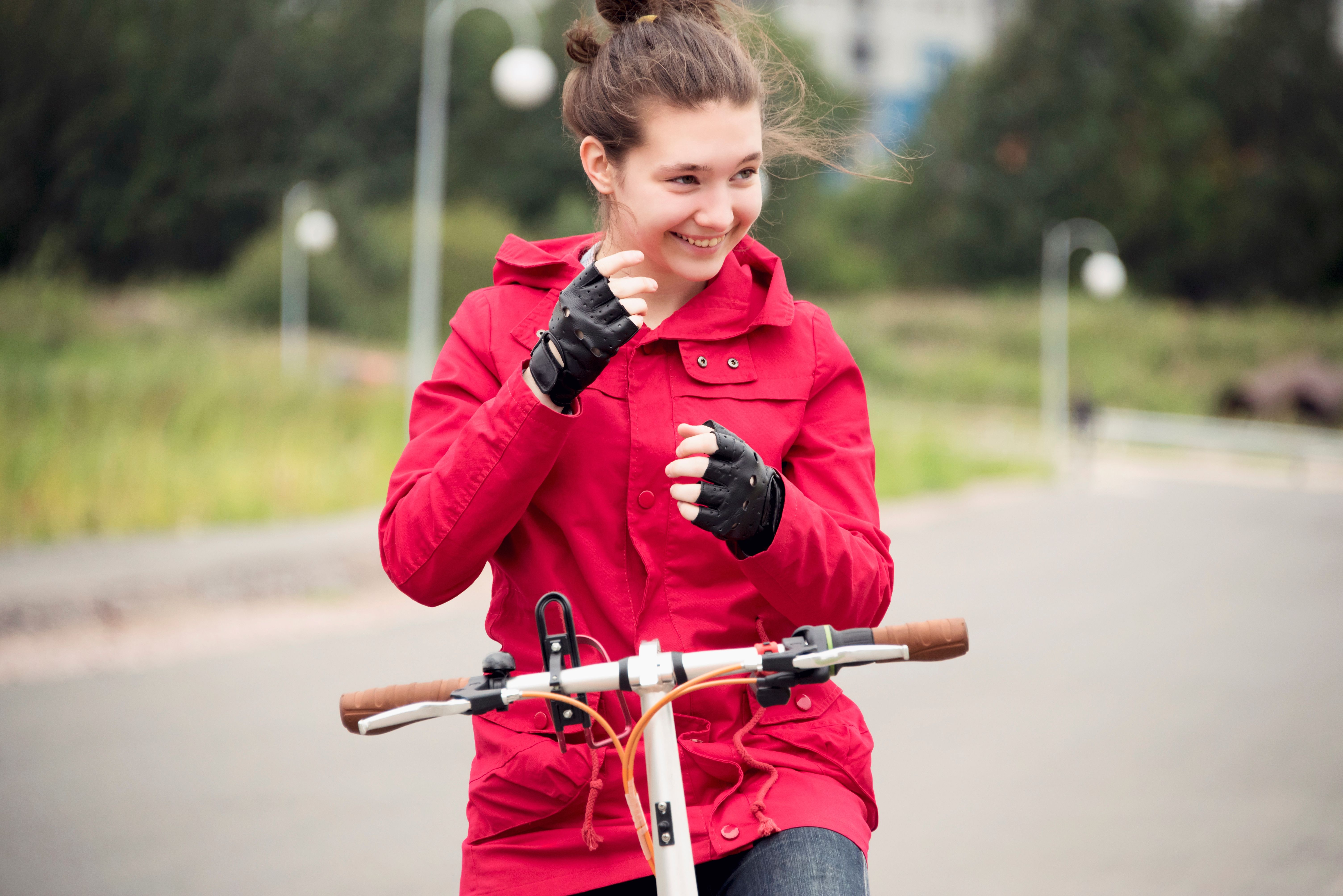 A smiling woman in a red shirt and gloves riding a bike with trees and lampposts in the background