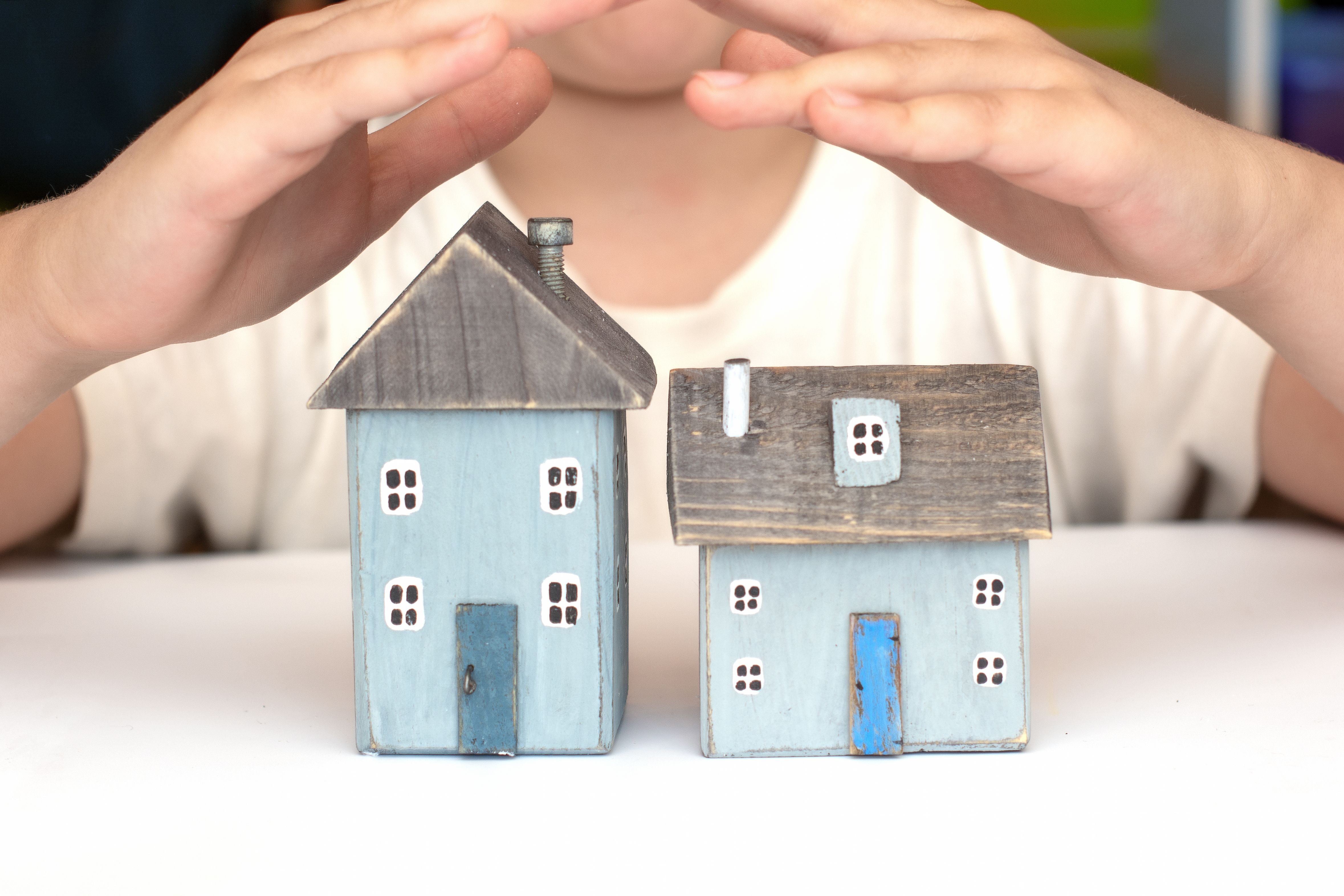  A man holding his hands above a model house in a gesture of support