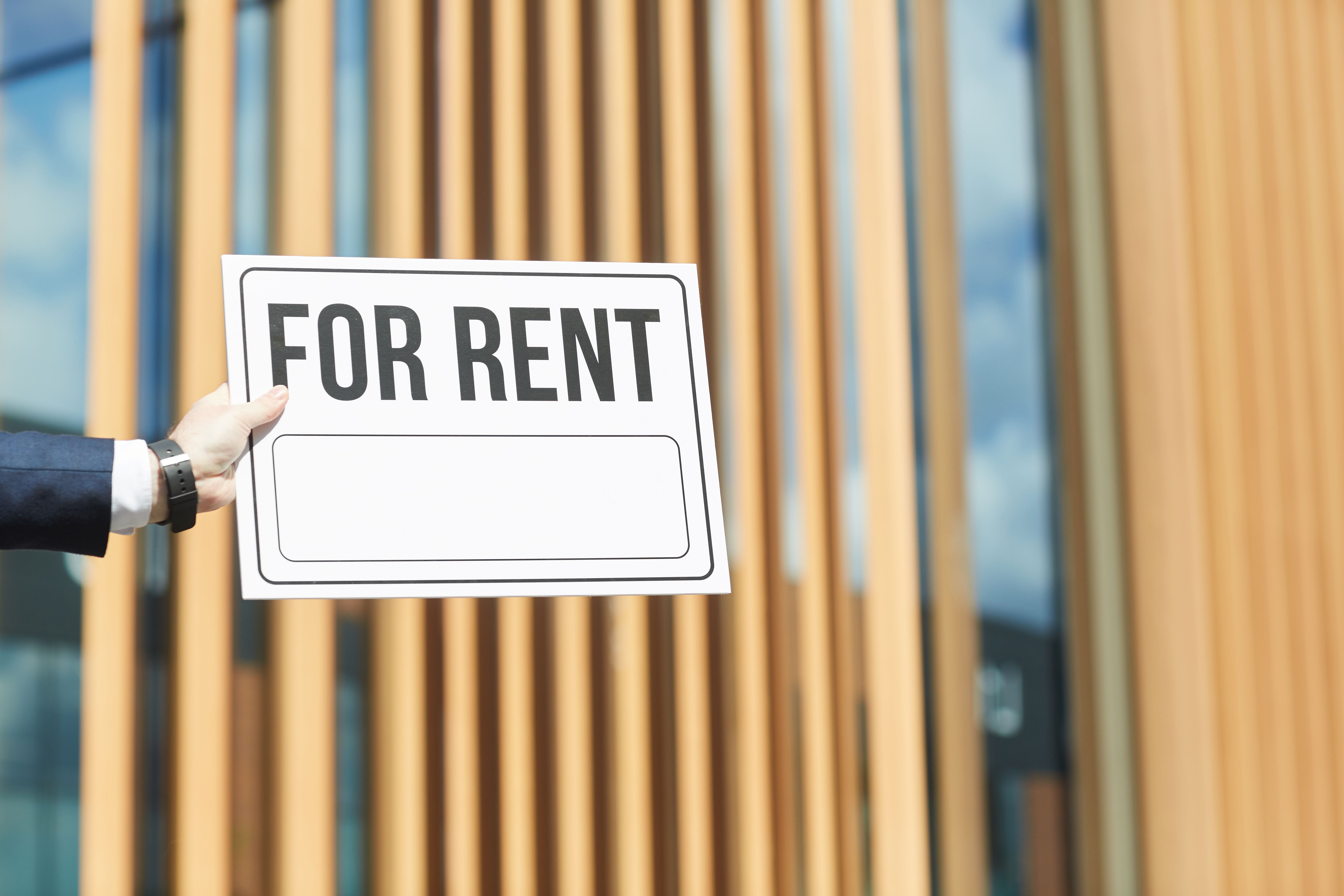 Close-up of a man holding placard “For Rent” against a building