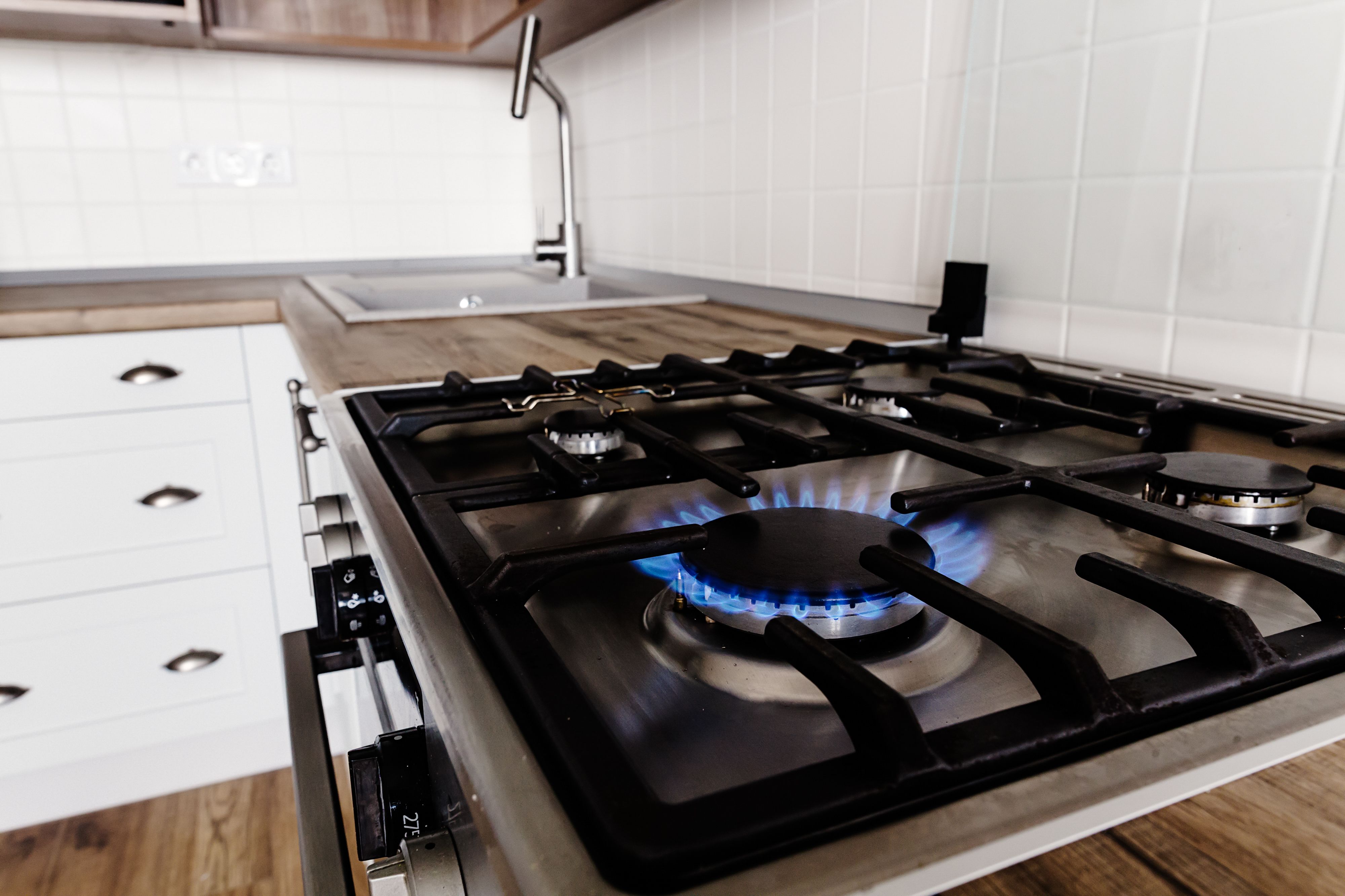 A gas hob with an open flame in a kitchen with wooden counter tops, a sink and white cabinets.JPG