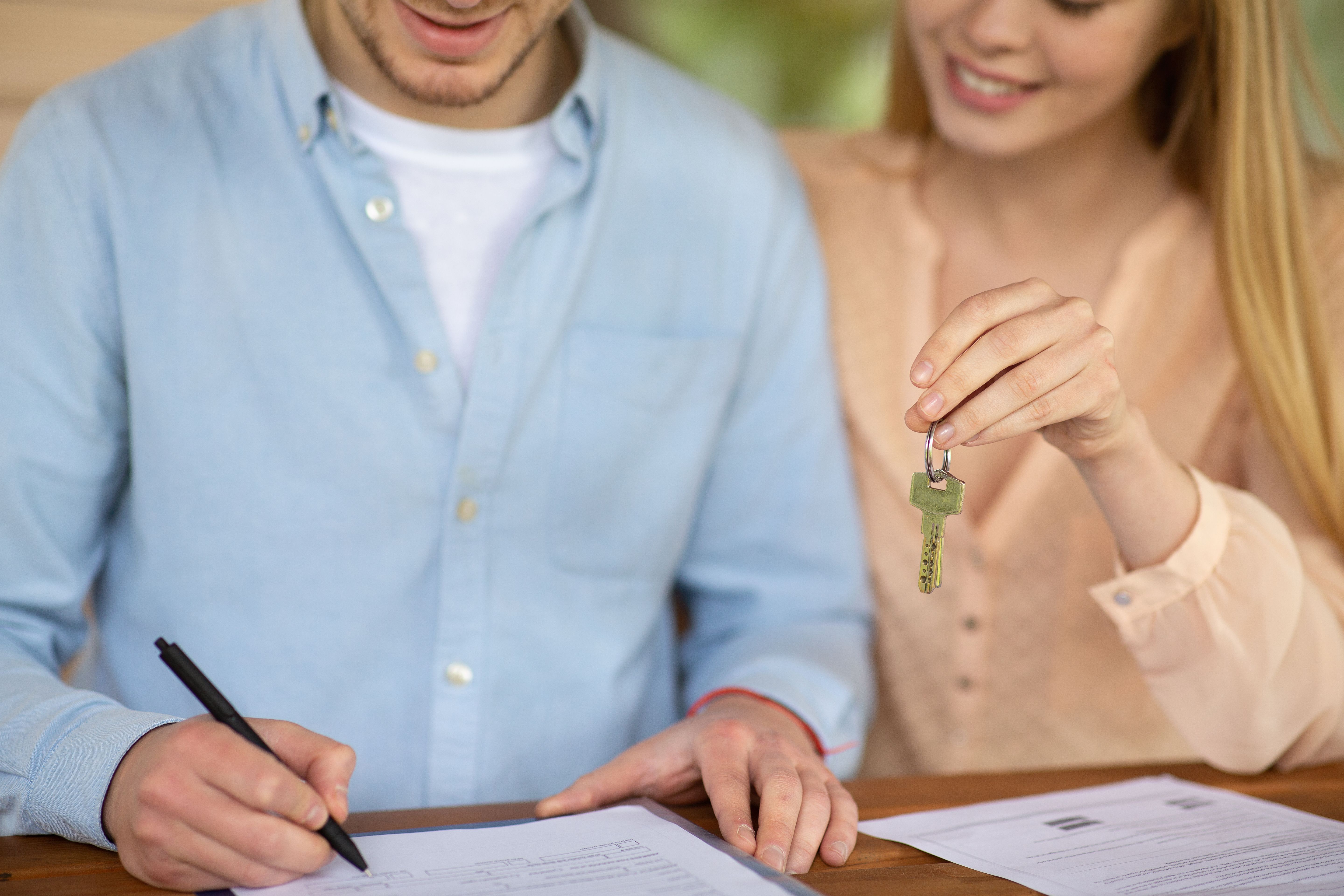 Closeup of a millennial couple signing a tenancy agreement while holding the keys to their new home
