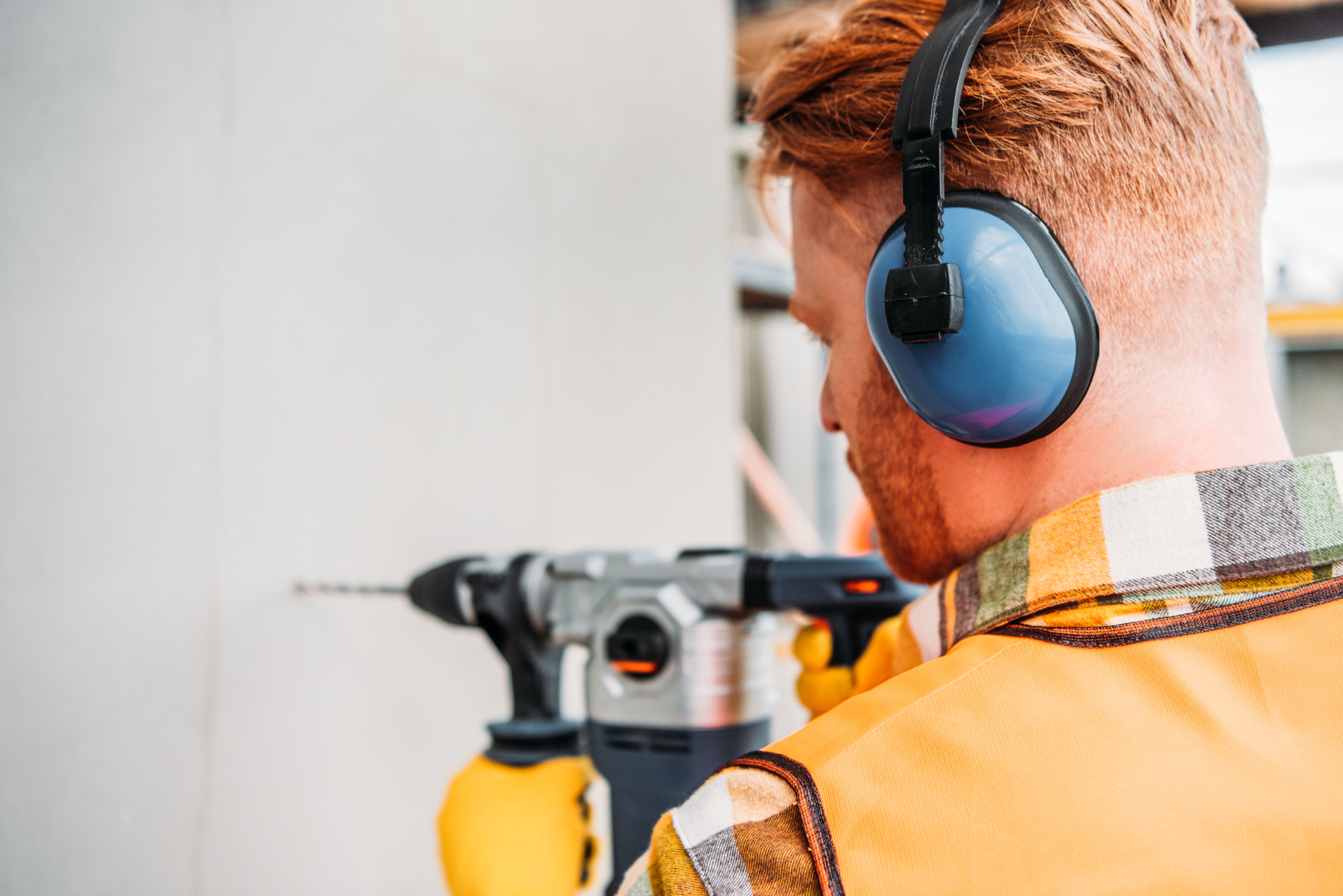 A repairman in noise-reducing headphones using a power drill