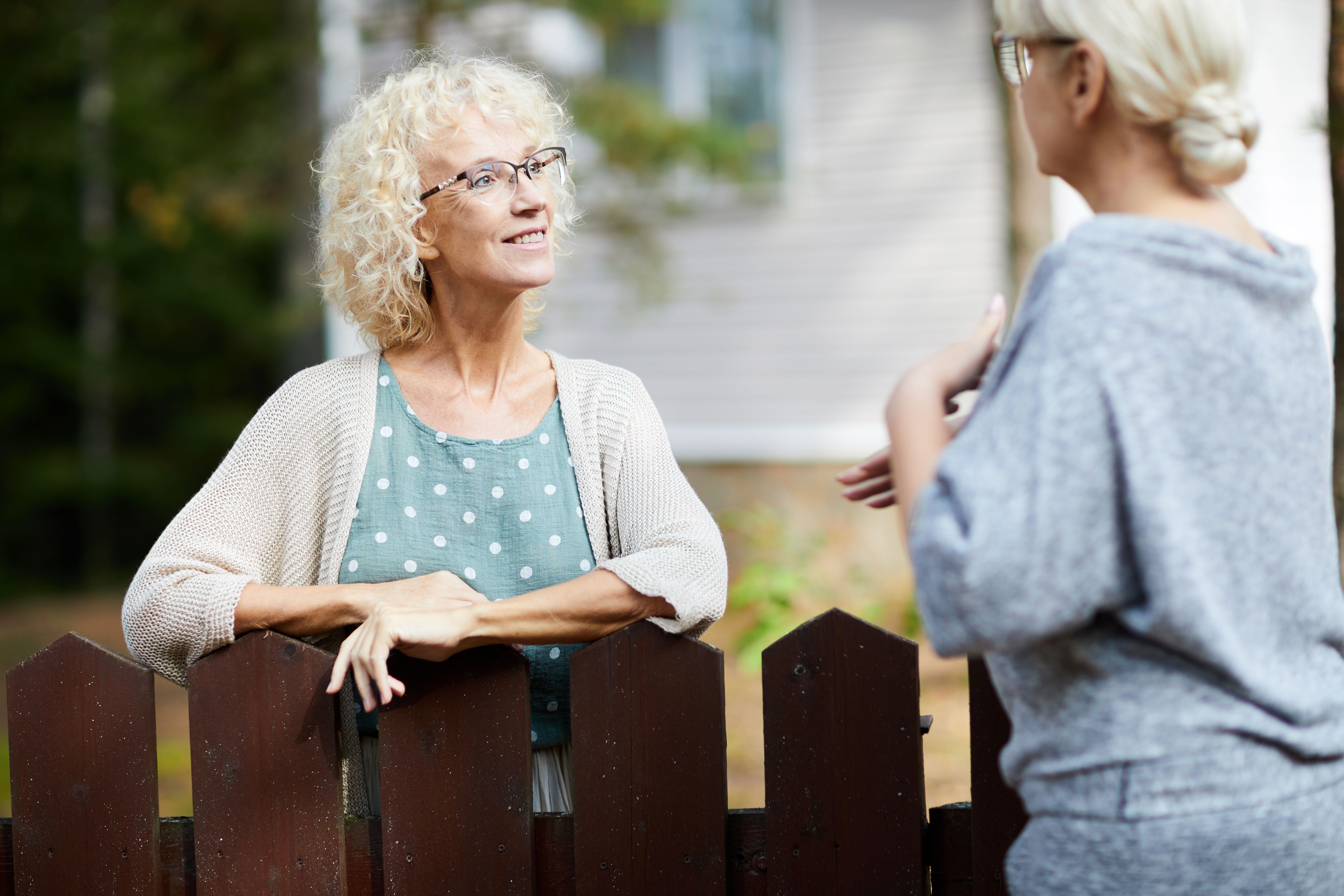 Two mature female neighbours talking through a fence