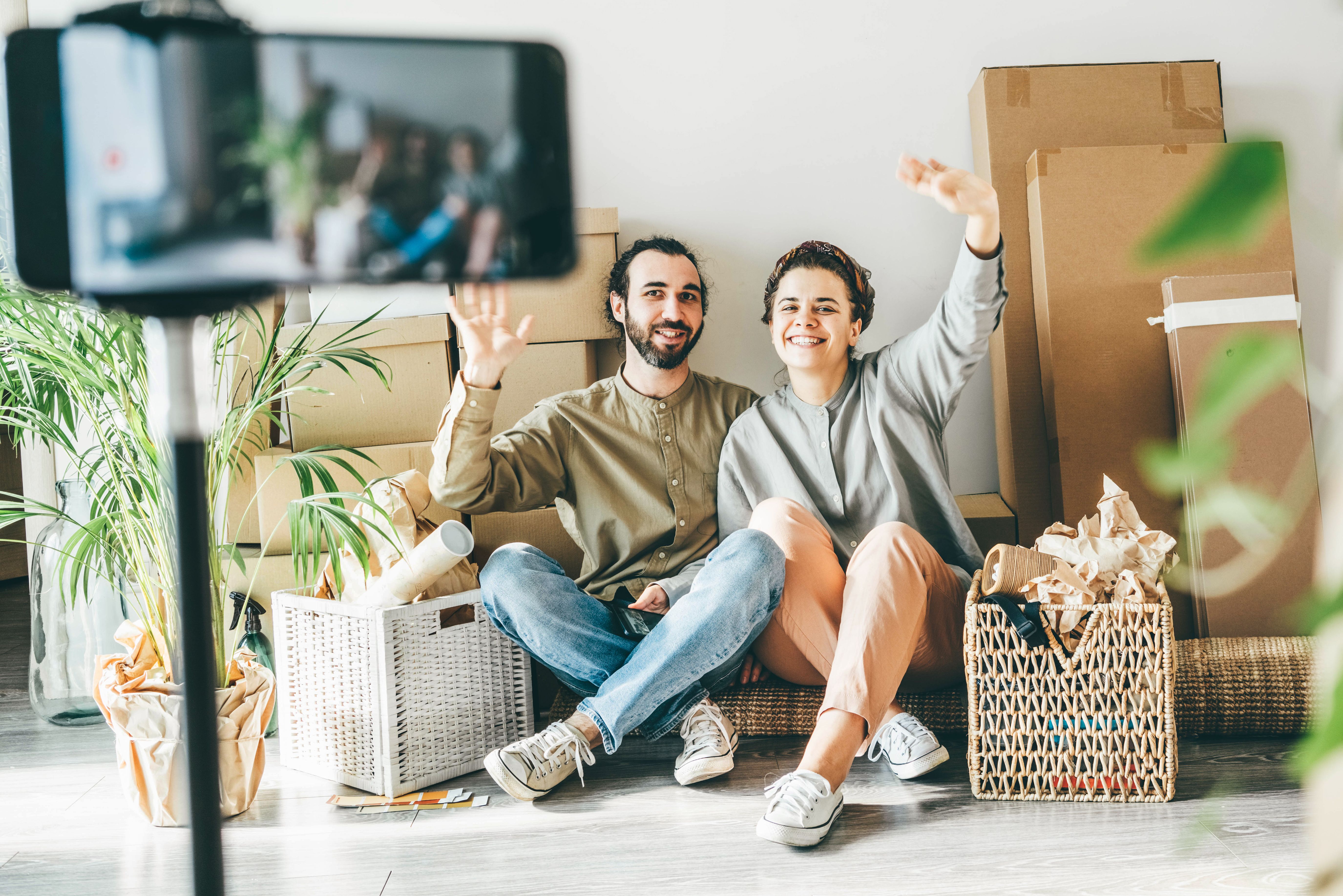 A happy couple sitting in the middle of boxes and plants, having just moved into their fully furnished Build To Rent apartment.