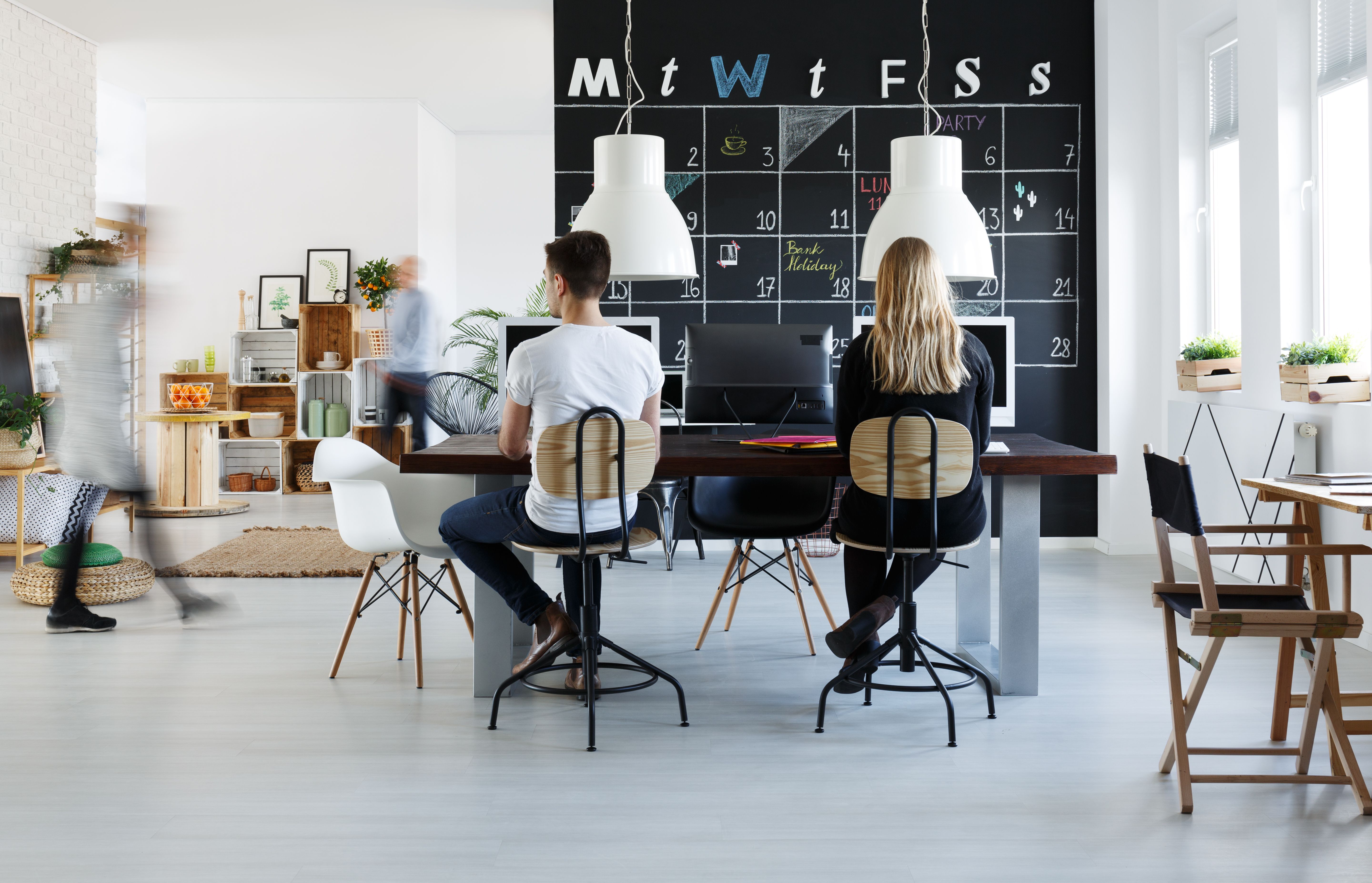 Freelancers in a co-working space with desks, chairs, plants and a calendar on the wall 