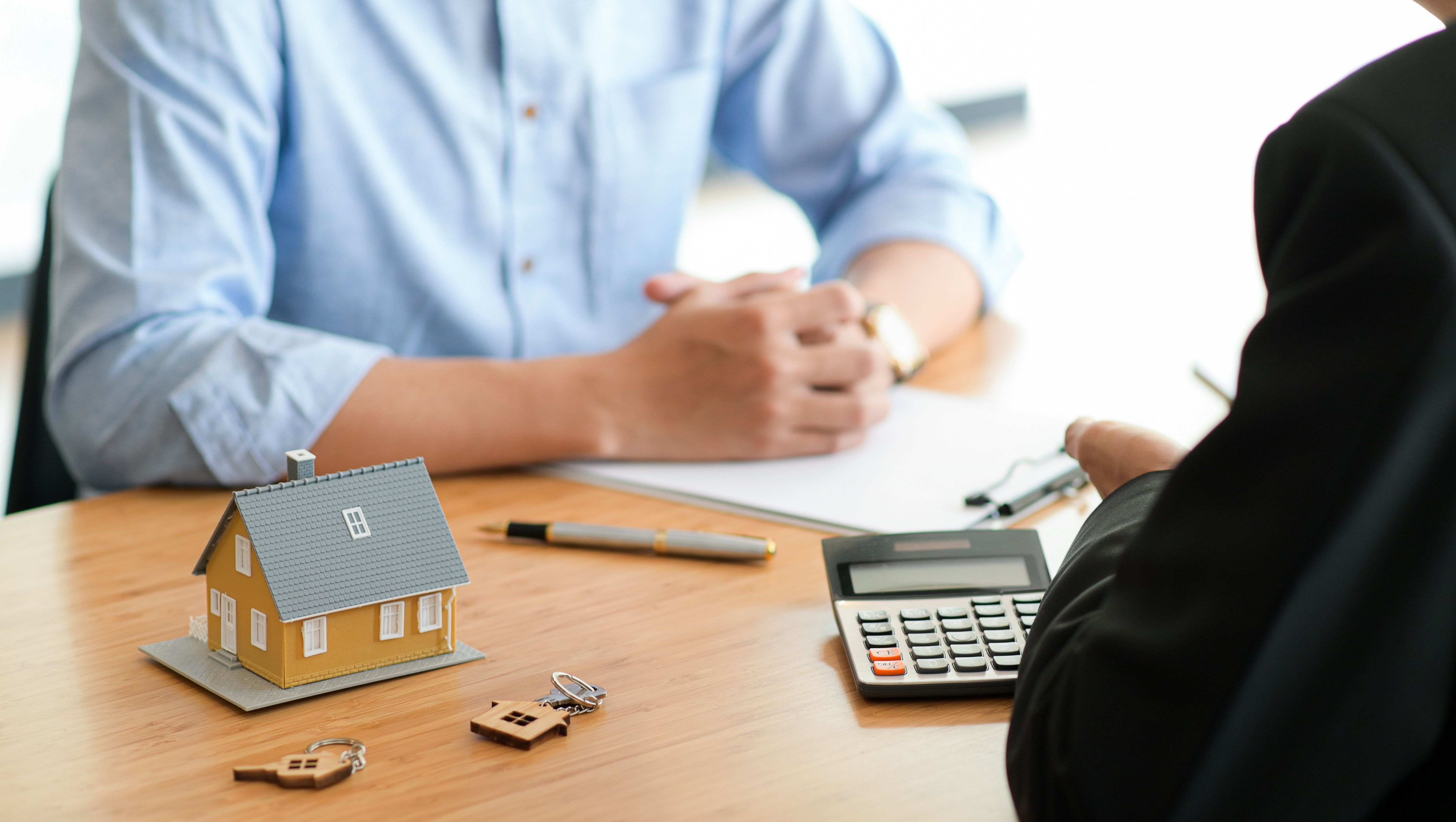 two people are in conservation, a computer and mini house model on the desk