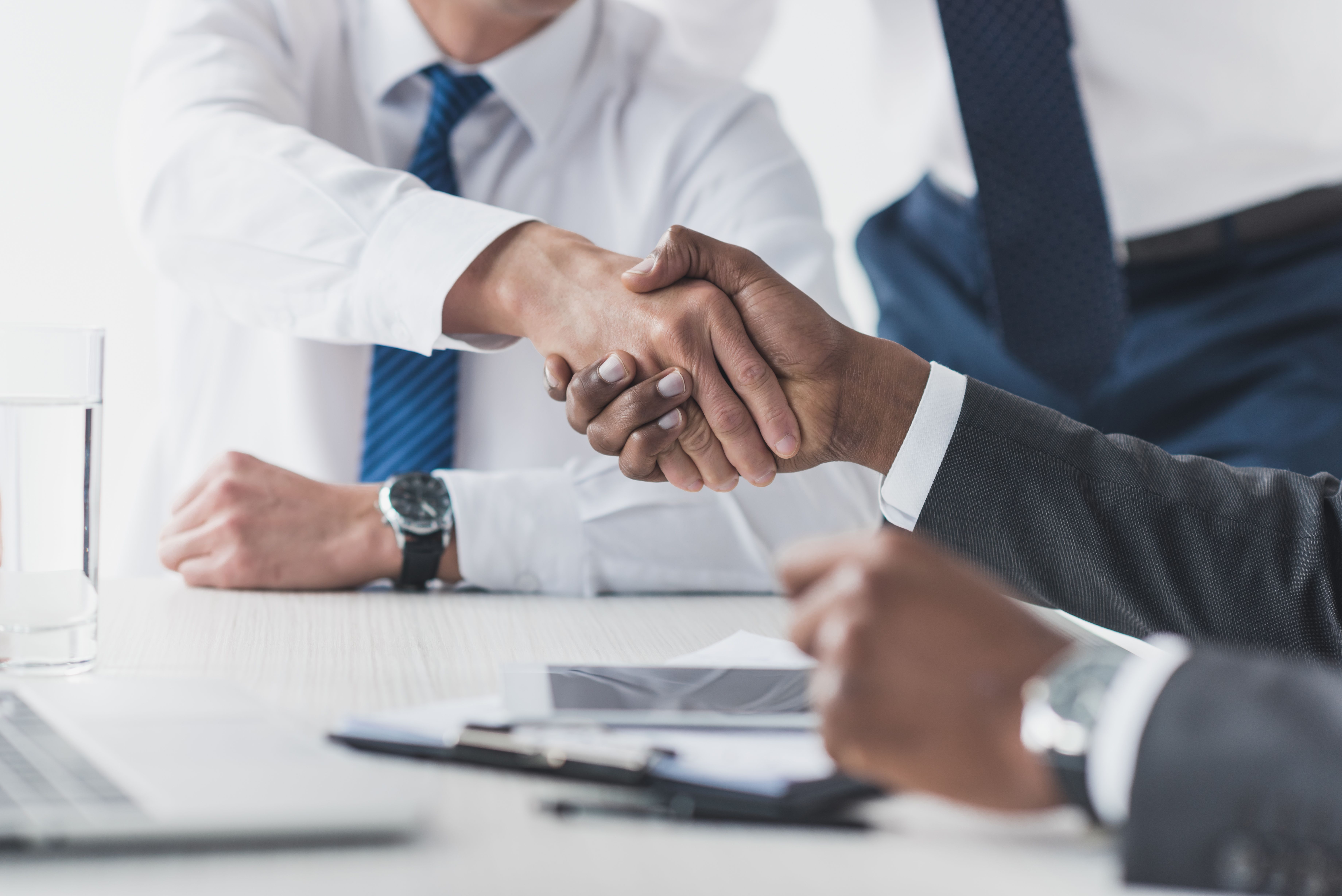 cropped shot of multicultural businessmen shaking hands while signing a contract in the workplace